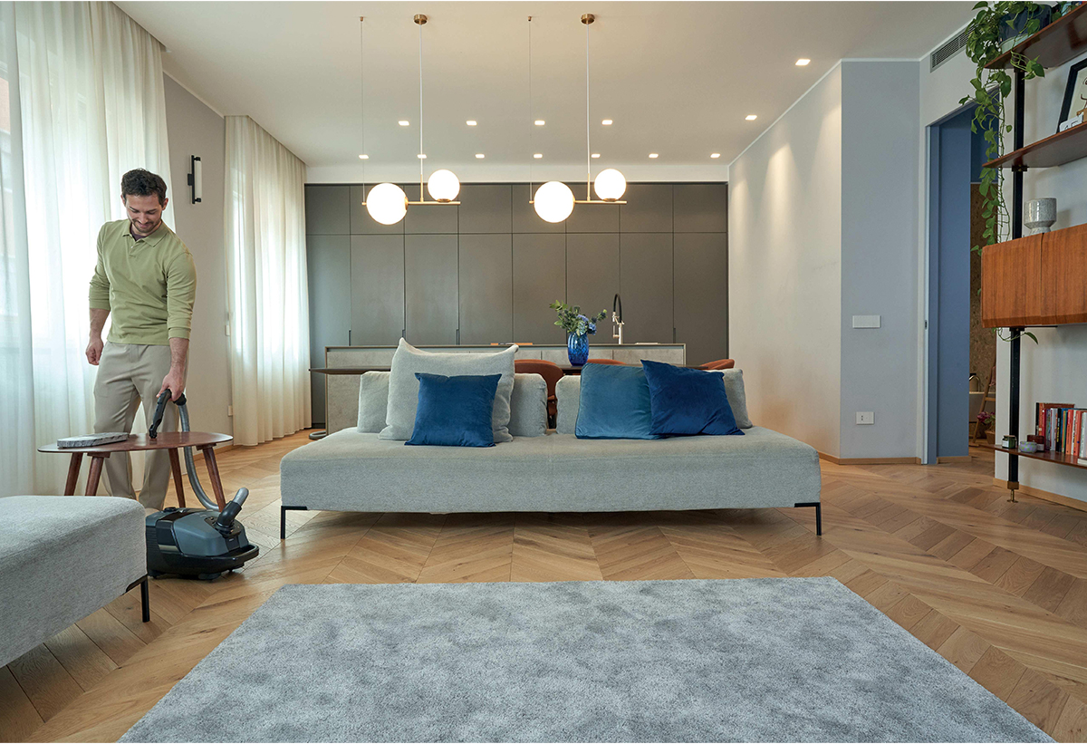 Απεικονίζεται άντρας να καθαρίζει τραπεζάκι σε σαλόνι με τη σκούπα.